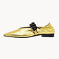 Gold metallic flat shoe with black flower detail on a white background