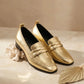 Pair of gold loafers on a beige surface with decorative elements.