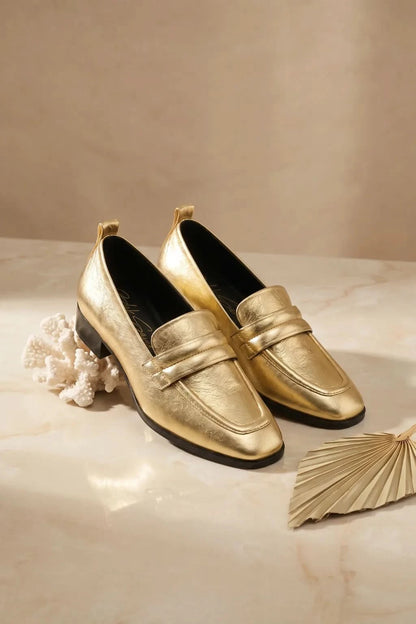 Pair of gold loafers on a beige surface with decorative elements.